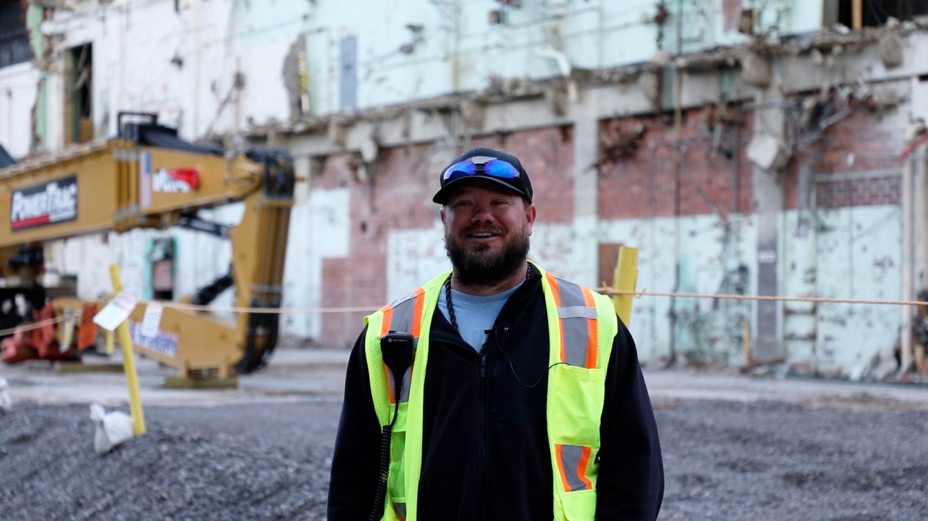 A man in protective gear smiles for a photo outside of a facility building