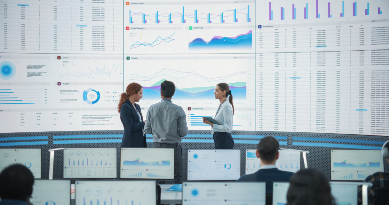 Three people stand before a large screen of data to discuss potential threats and risks.