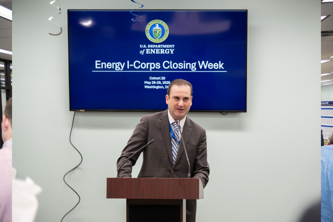 A man stands in front of a podium to address a group of people.  