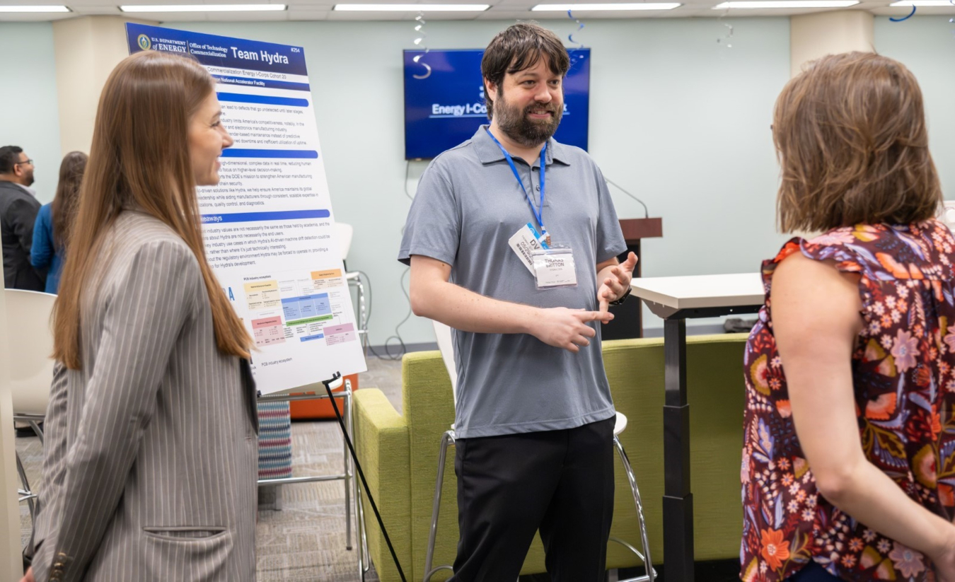 A woman and a man standing next to a project poster and conversing with a woman viewing the poster.