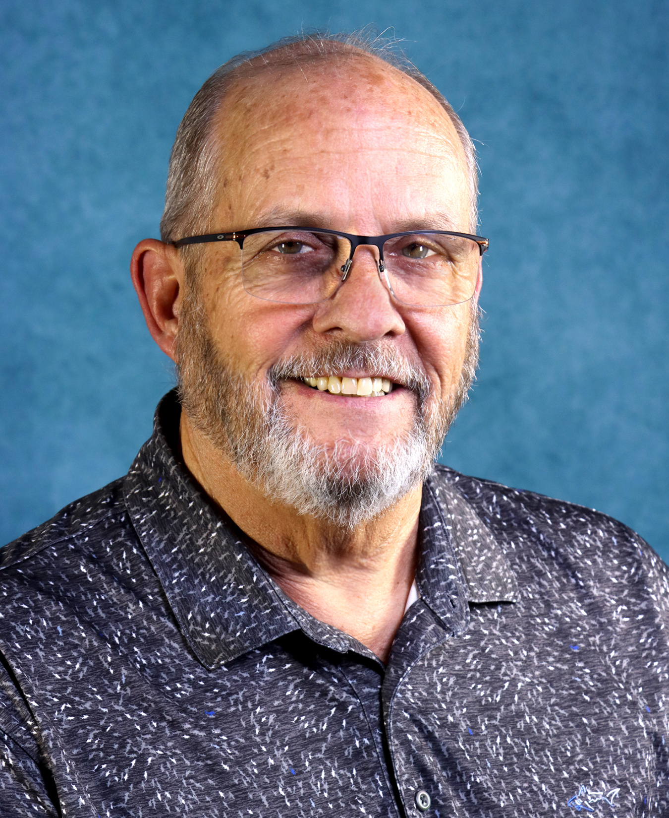 Professional headshot of a man in a dark patterned shirt