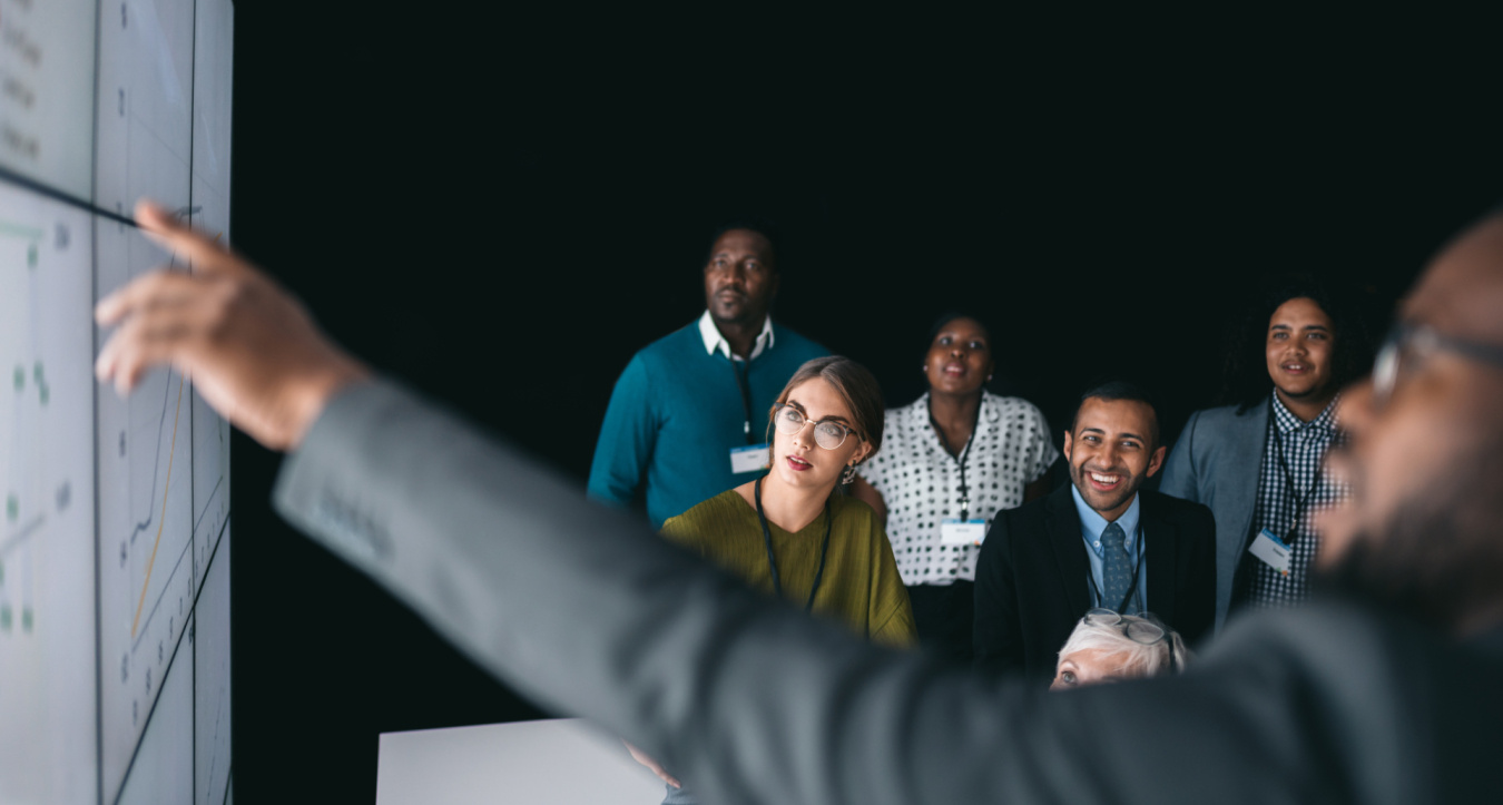 A man points to a diagram of information in front of an audience.