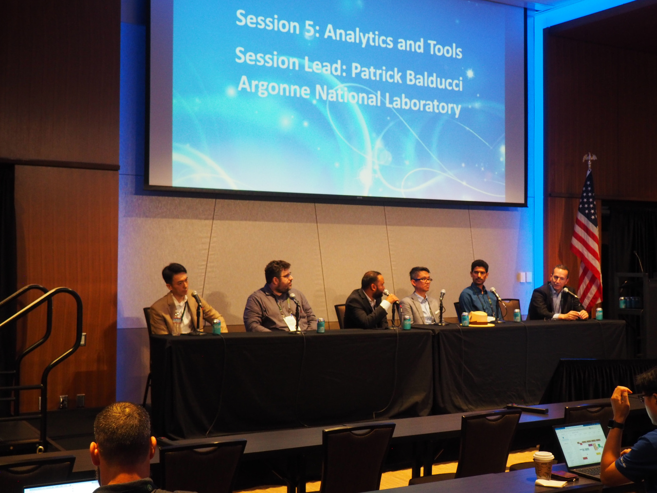 Six people sit on a panel at the 2024 OE Energy Storage Annual Meeting and Peer Review with a large screen overhead. 