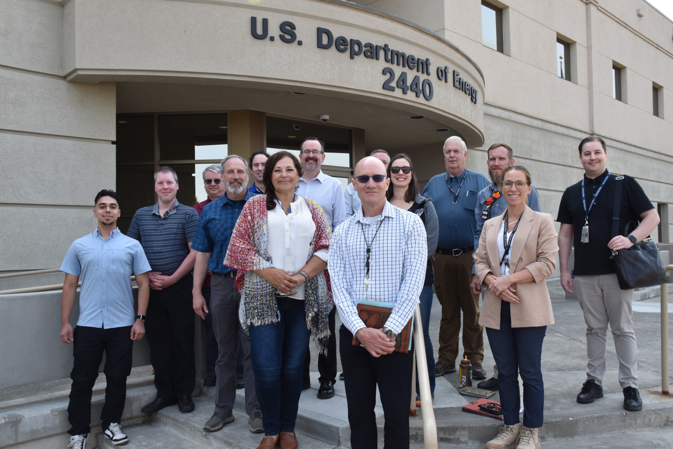 A group of people outside the Department of Energy building smiling for a group photo