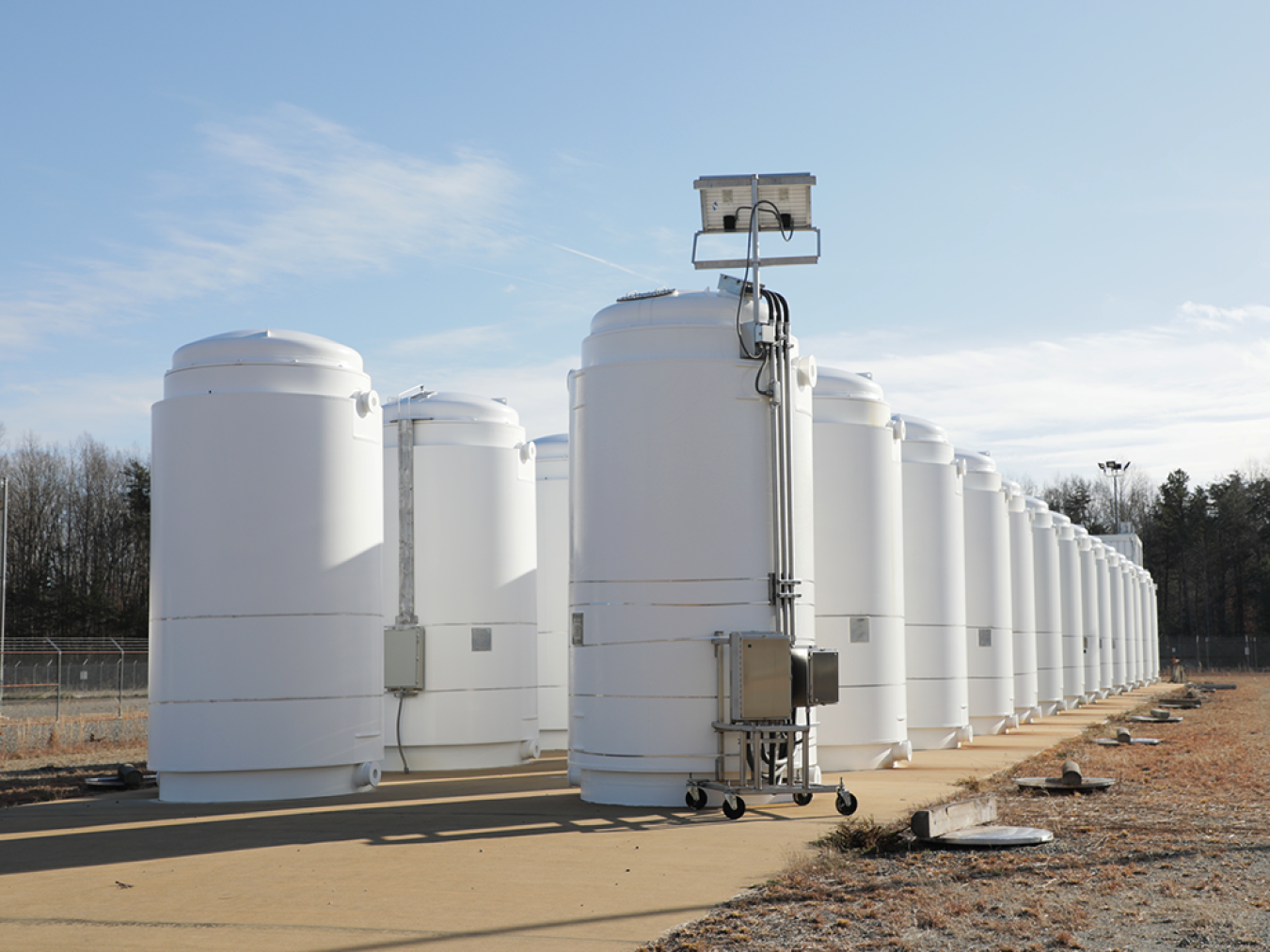 Two rows of tall white cylinders on a concrete pad with a blue sky in the background.