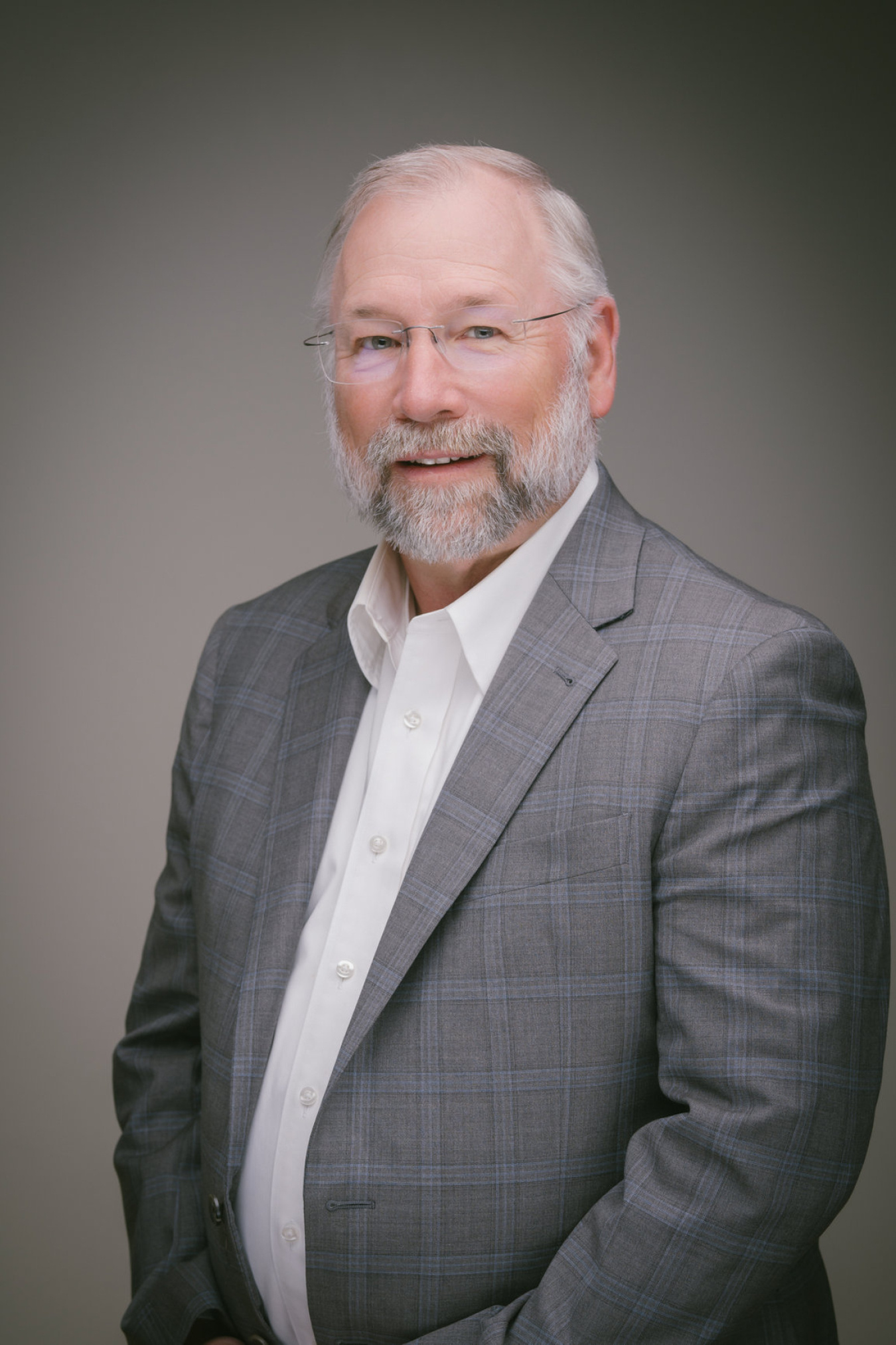 A professional headshot of a man in the grey suit jacket and white shirt