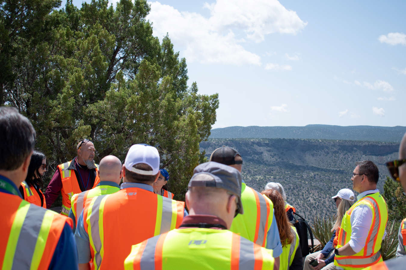 A group of people touring Los Alamos with a scenic overlook behind them