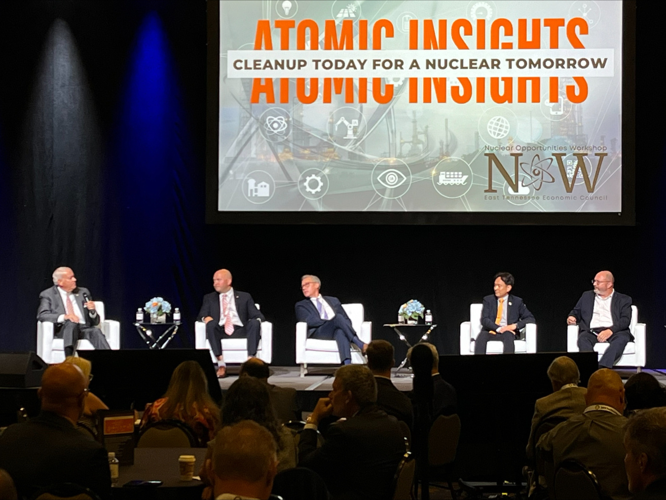 A panel of five individuals on stage at a conference event