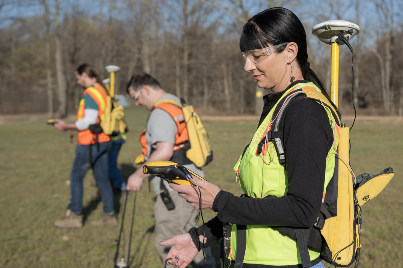 Three employees surveying land while wearing protective gear 