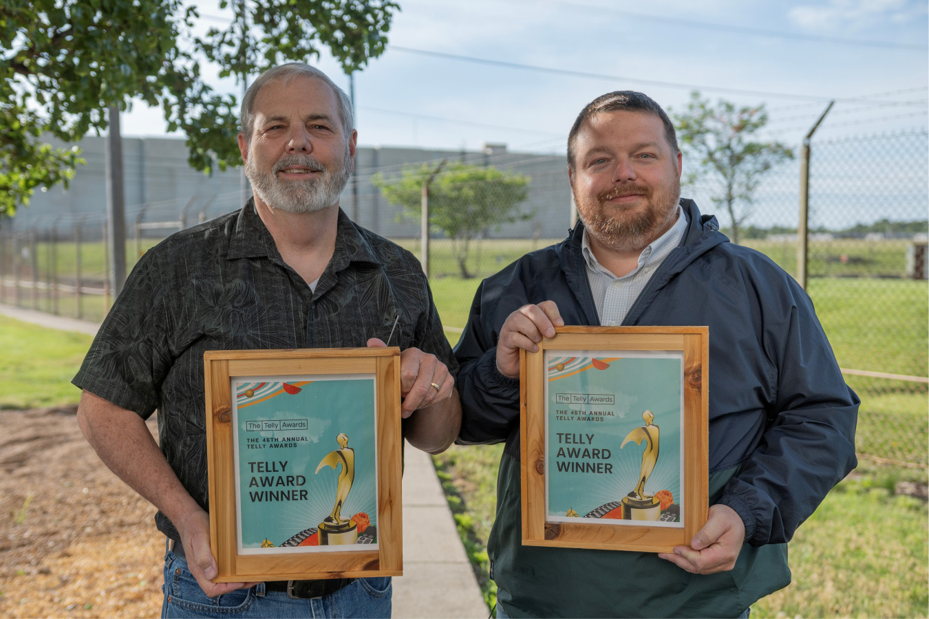 Two men smiling for a picture while holding awards in wooden frames