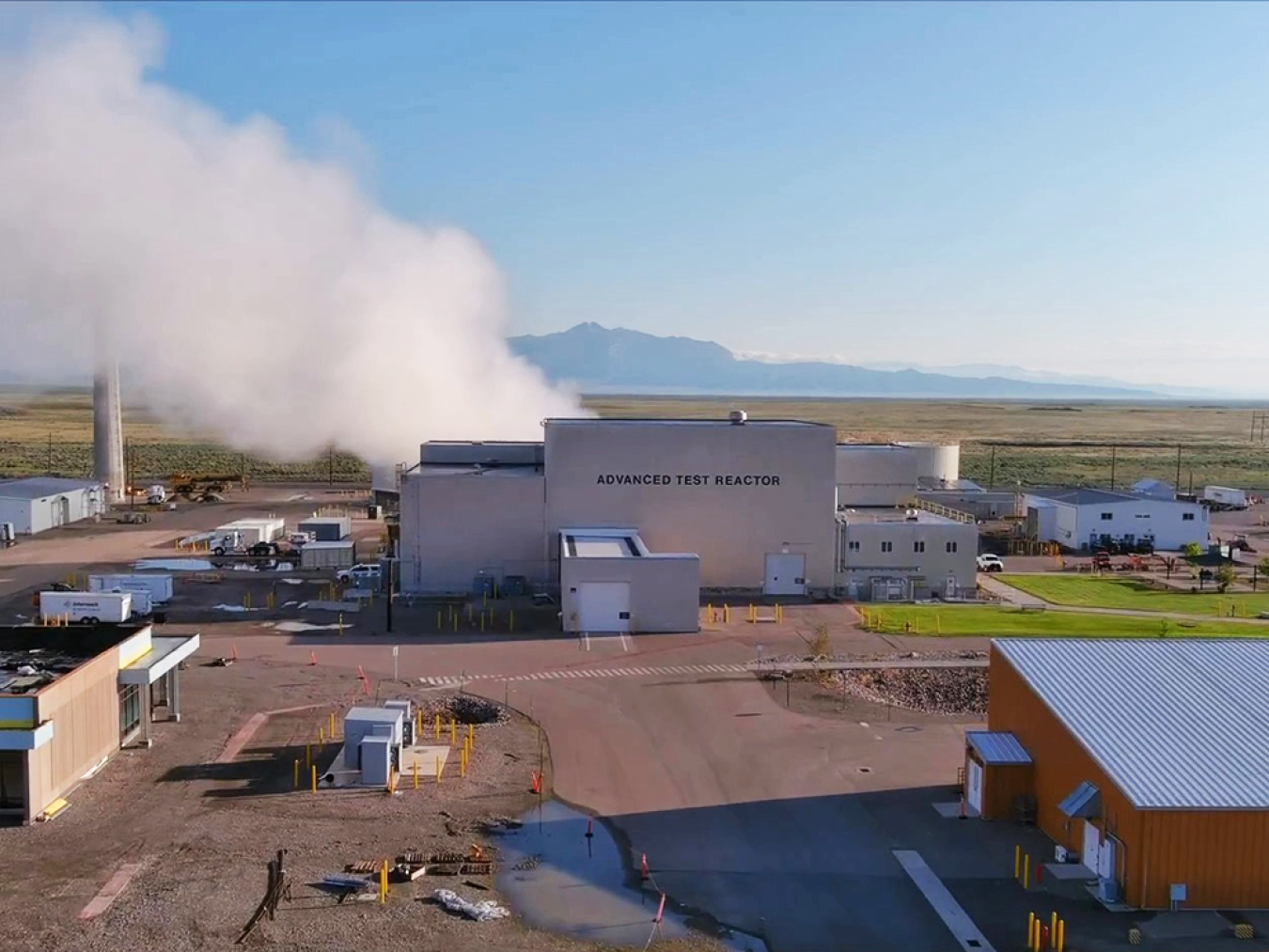Exterior view of the Advanced Test Reactor, a tall gray building with a column of steam rising from the left side.