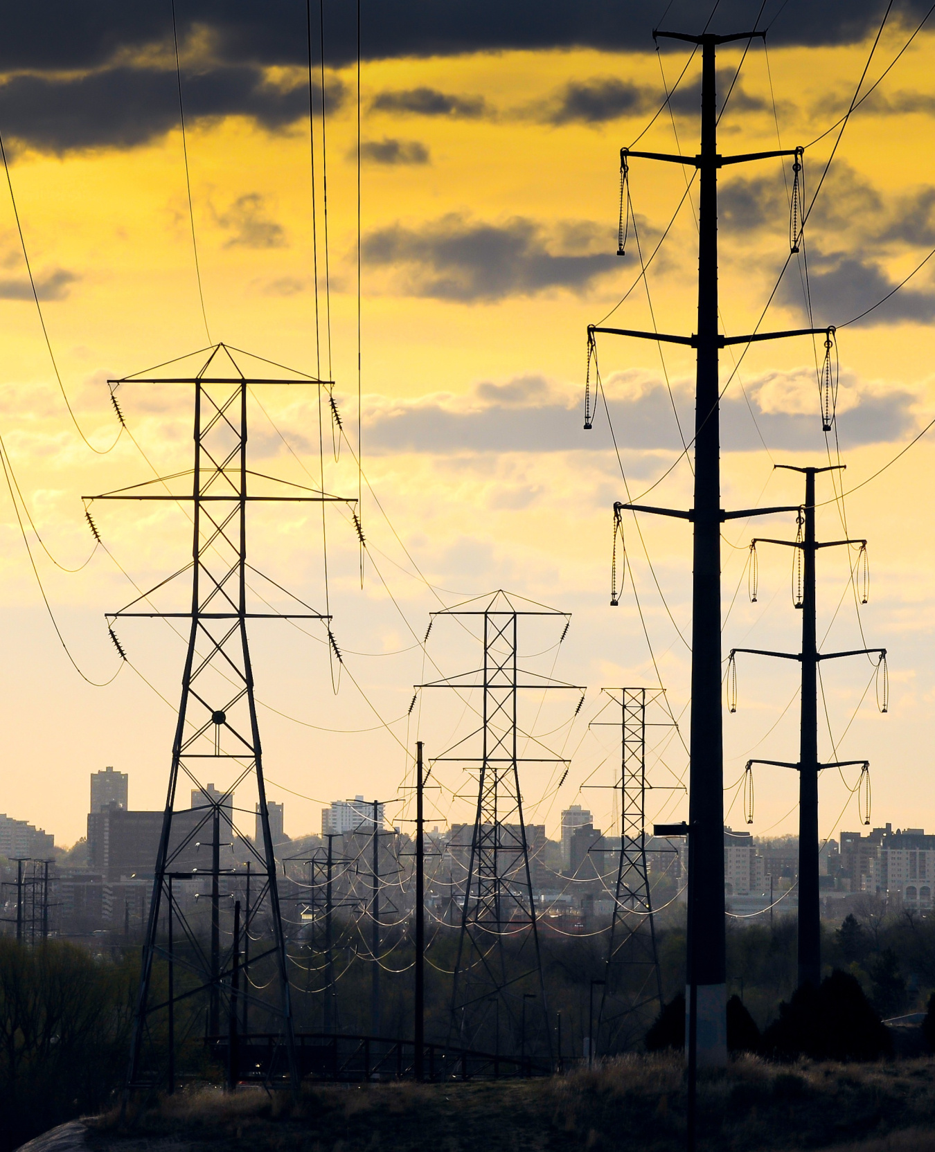 Two different types of transmission lines at sunset with the city of Denver skyline in the background.