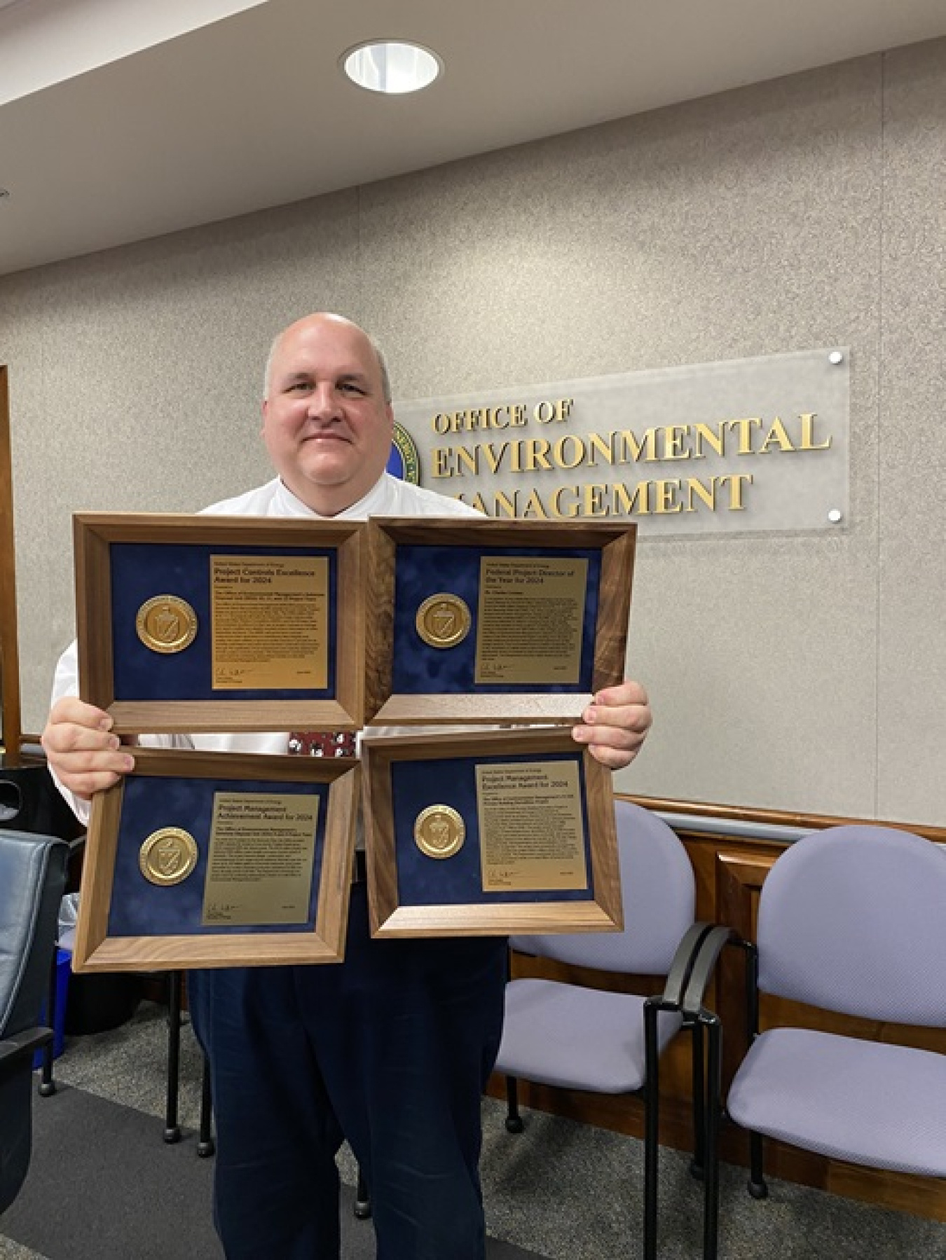 A man holding up four award plaques in a conference room