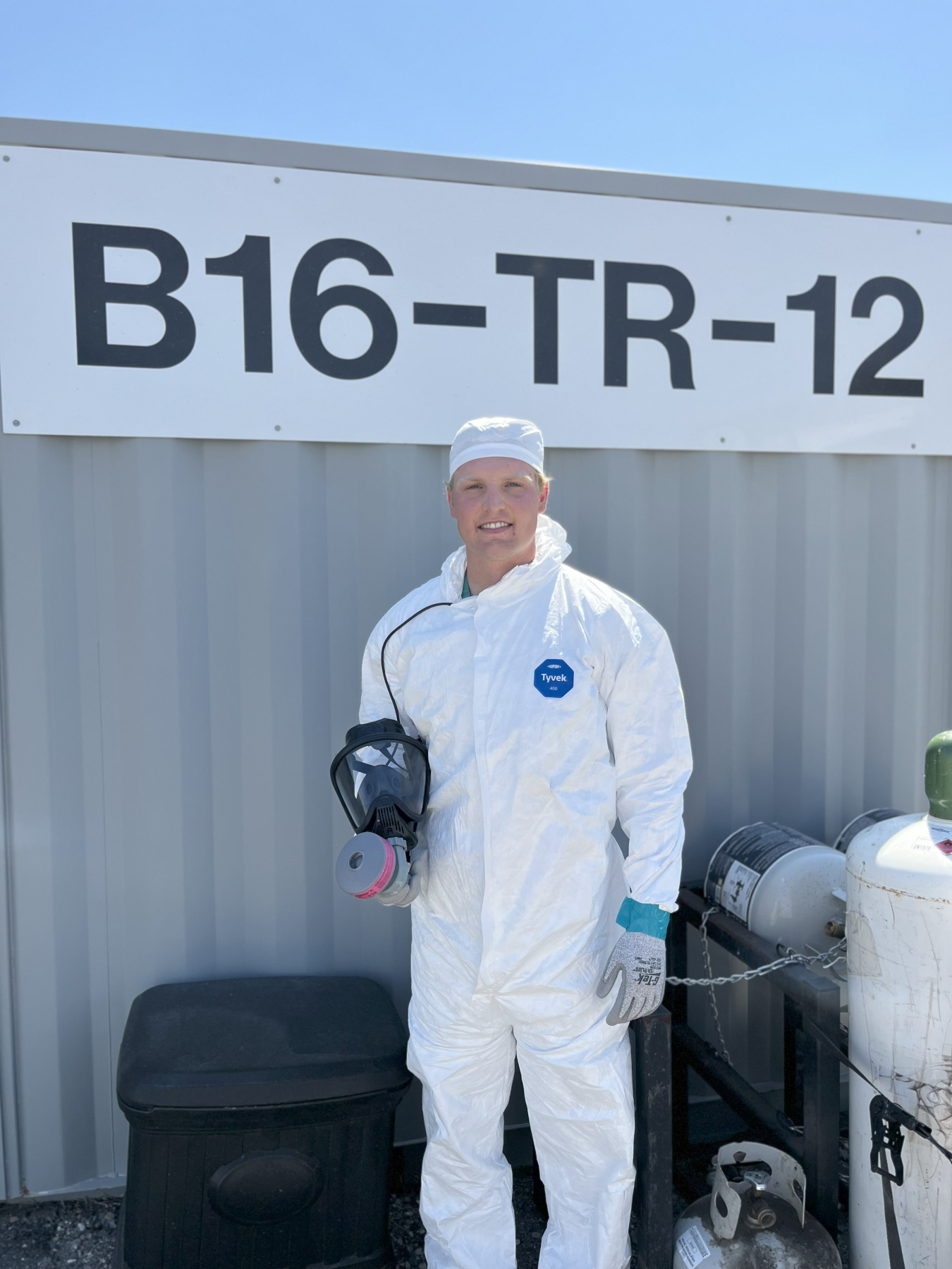 An intern in white safety protective gear stands outside of a building