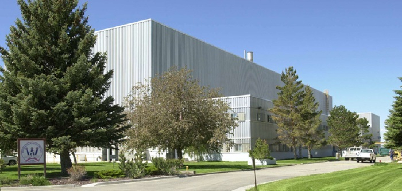 A large white facility building with trees and grass out front