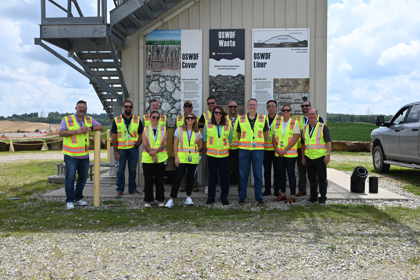 A group photo of individuals in yellow safety vests posing for a group picture outside of a building 