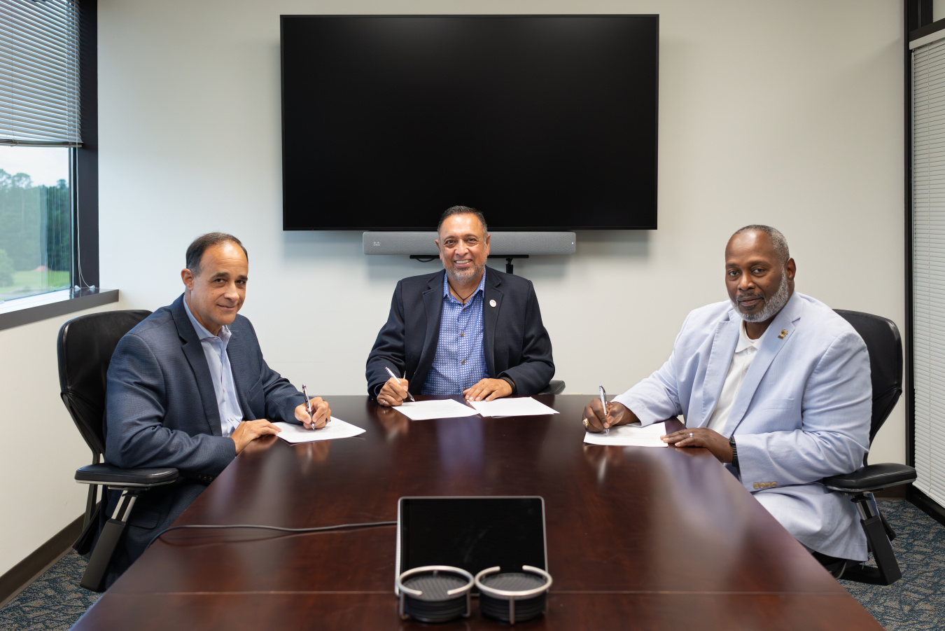 Three professionals sitting at a conference table posing for a group photo