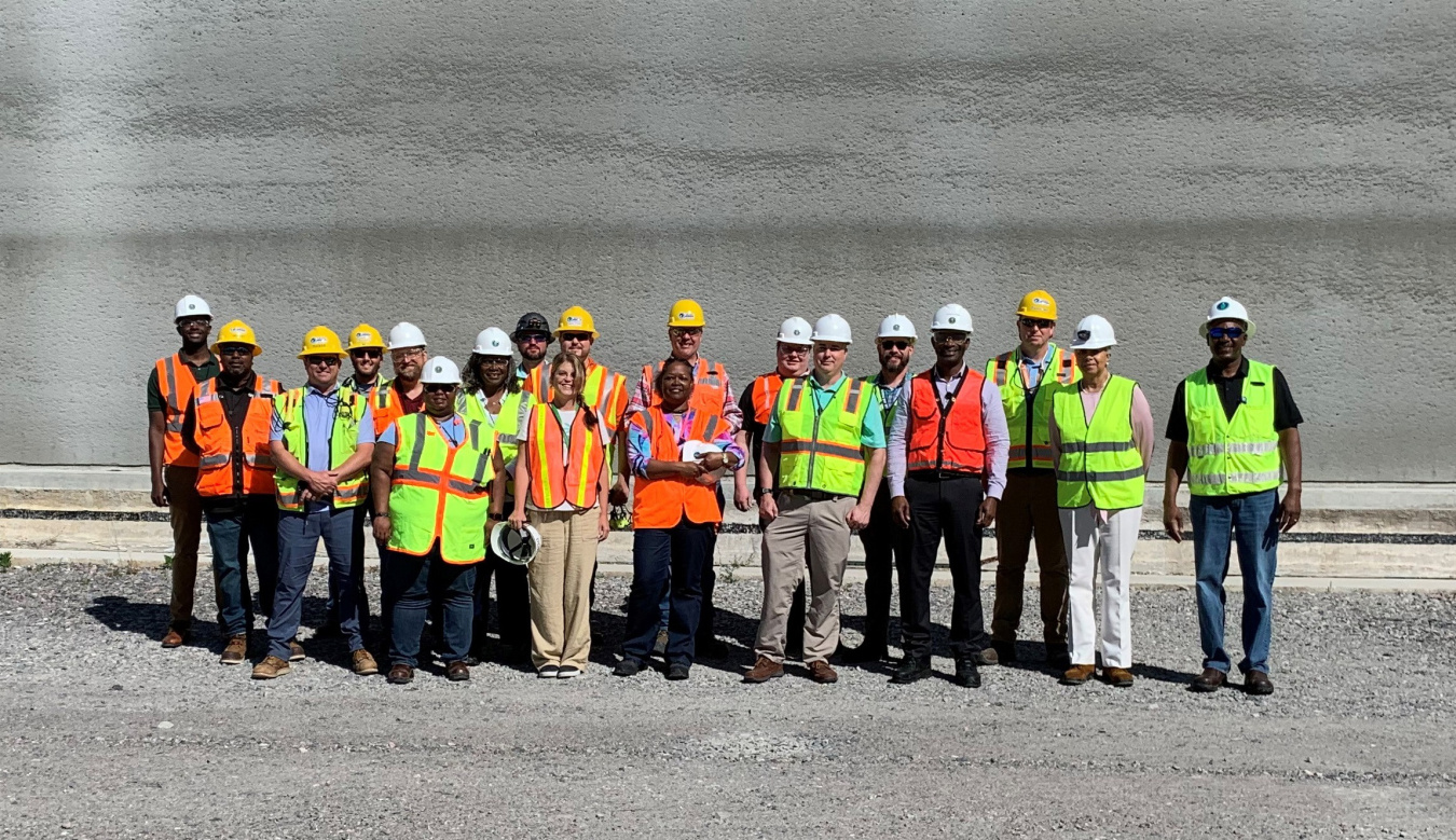 A group picture of employees in safety vests and hard hats outside of a disposal unit