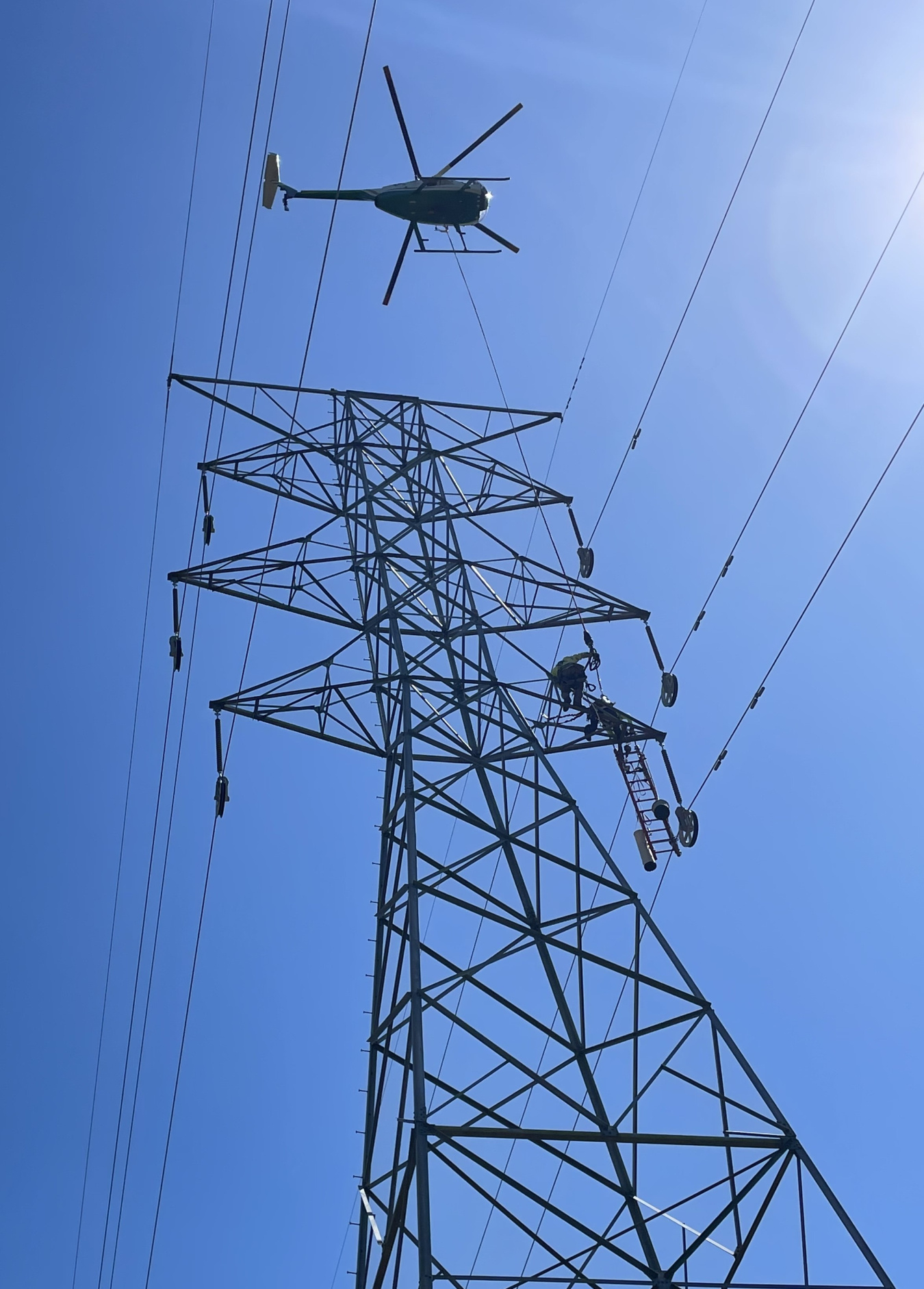 helicopter over transmission tower and lines. blue sky in background.