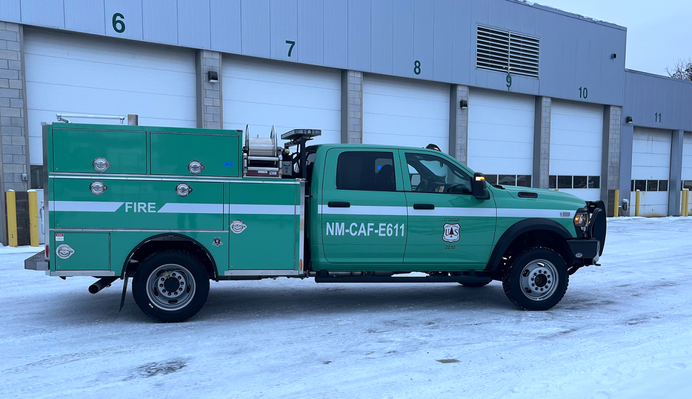 A green federal fleet truck in front of a garage building with multiple bays.