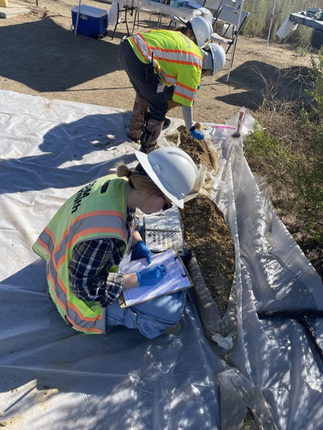 Employees in protective gear inspecting rock materials outside