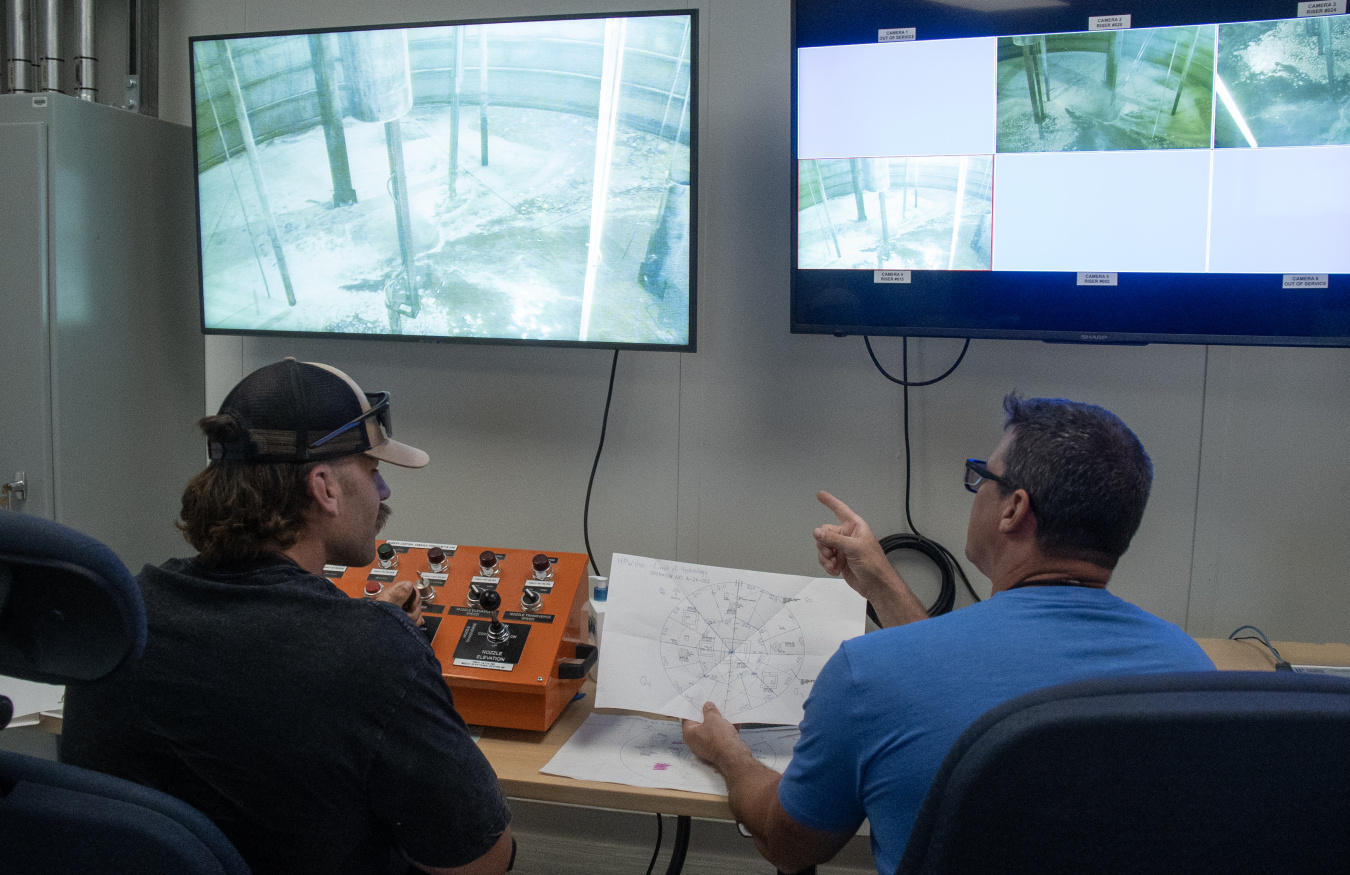 Two employees sitting in front of two monitors displaying the inside of a tank