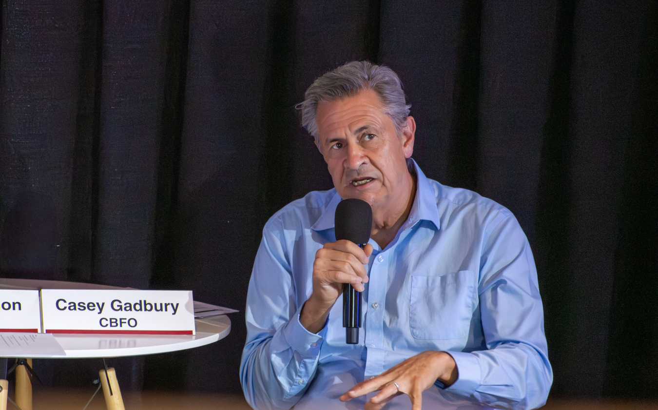 A man holding a microphone while sitting down speaking to a crowd