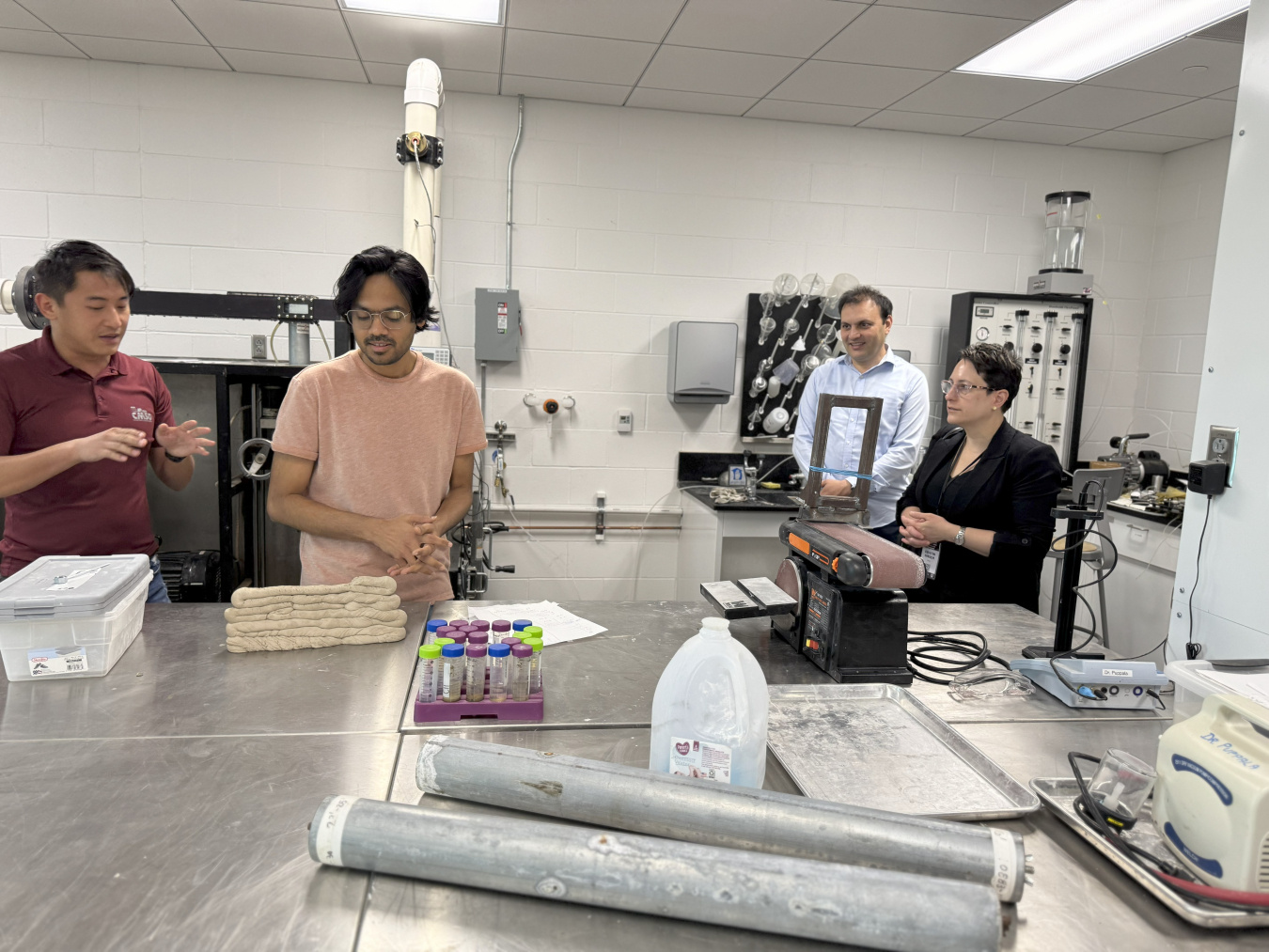 In a lab settling, a person in a maroon shirt explains how the various objects on a table -- test tubes, equipment, etc. -- used in eBeam work.