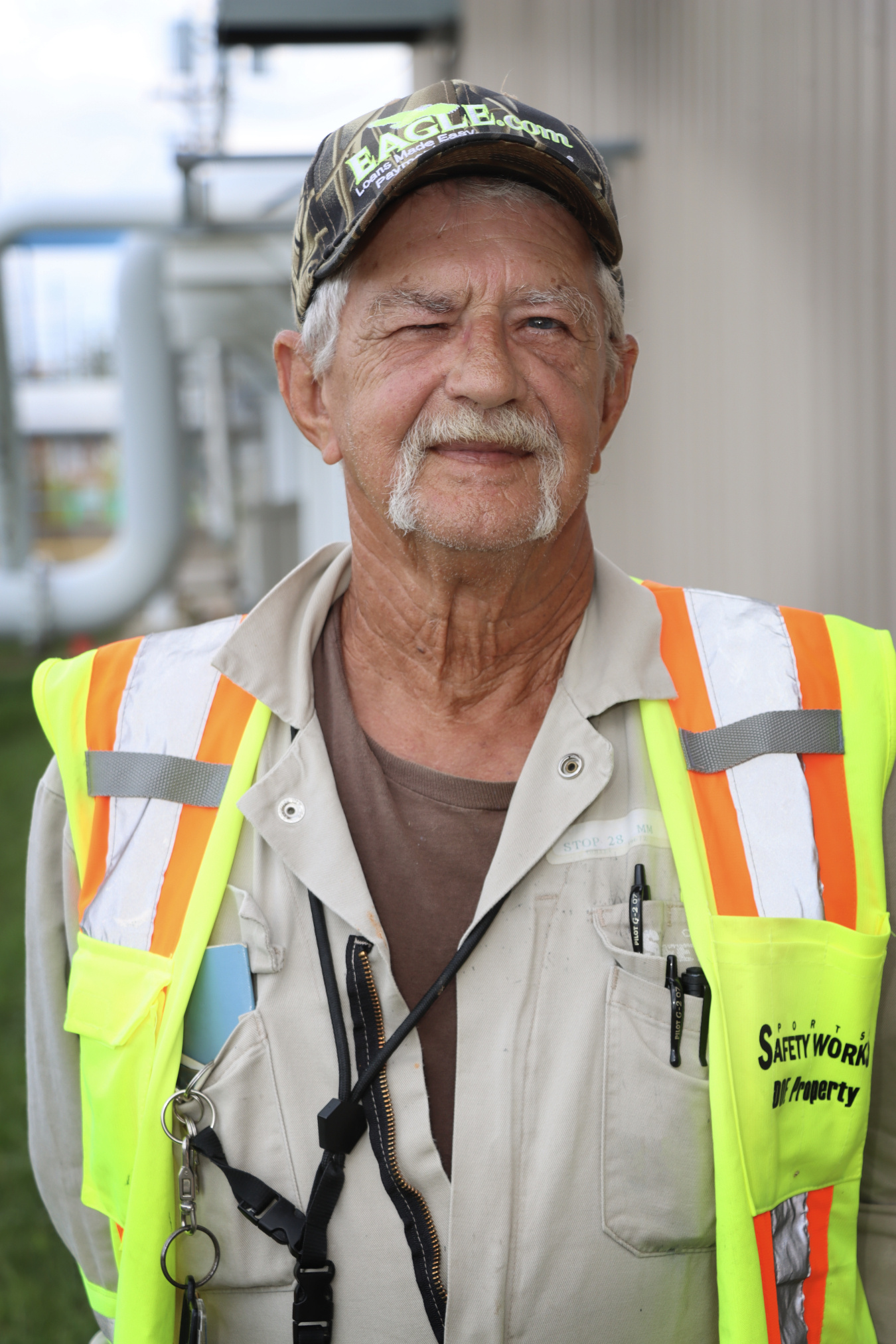 A smiling man wearing a yellow safety vest and a camo hat
