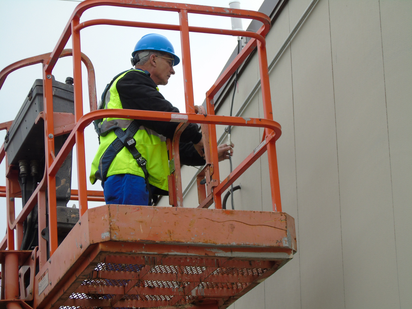 A may in protective gear in a lift working on a building 