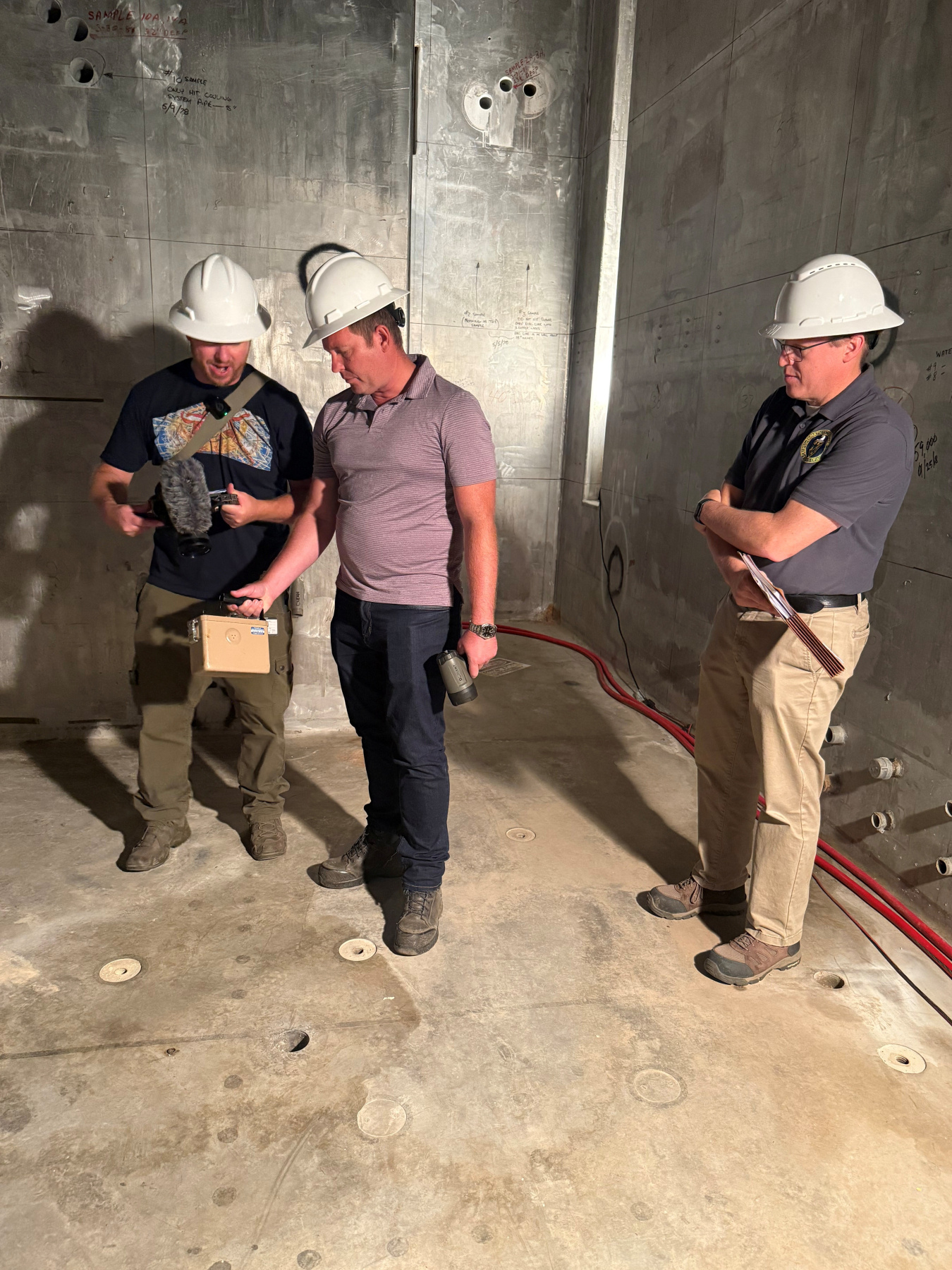 Three men take radiological readings and talk in basement