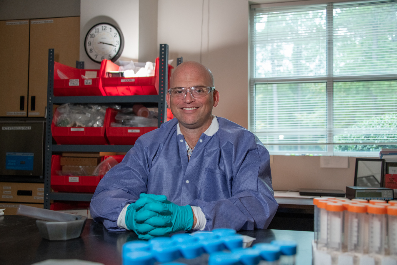 A scientist in a blue outfit with protective goggles inside a laboratory