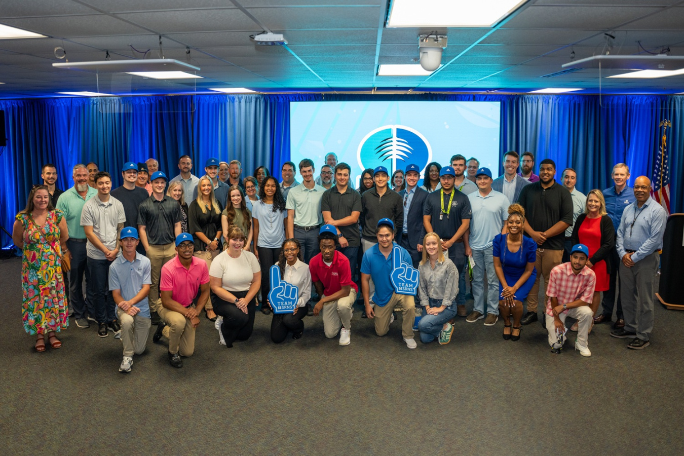 A large group of interns posing for a photo in front of a blue wall