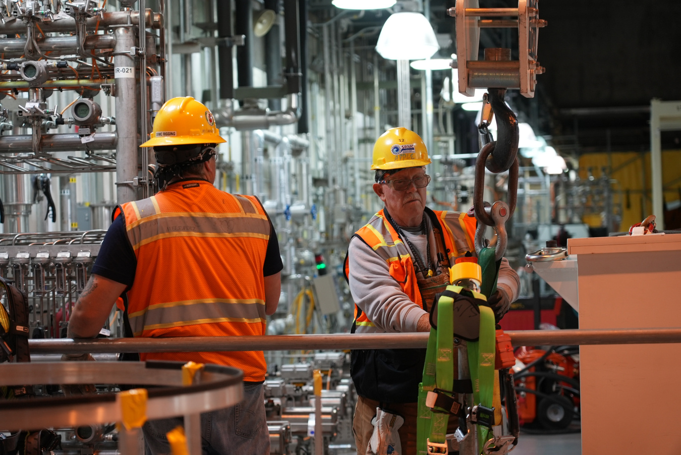 Two employees in protective gear working on a rigging machine