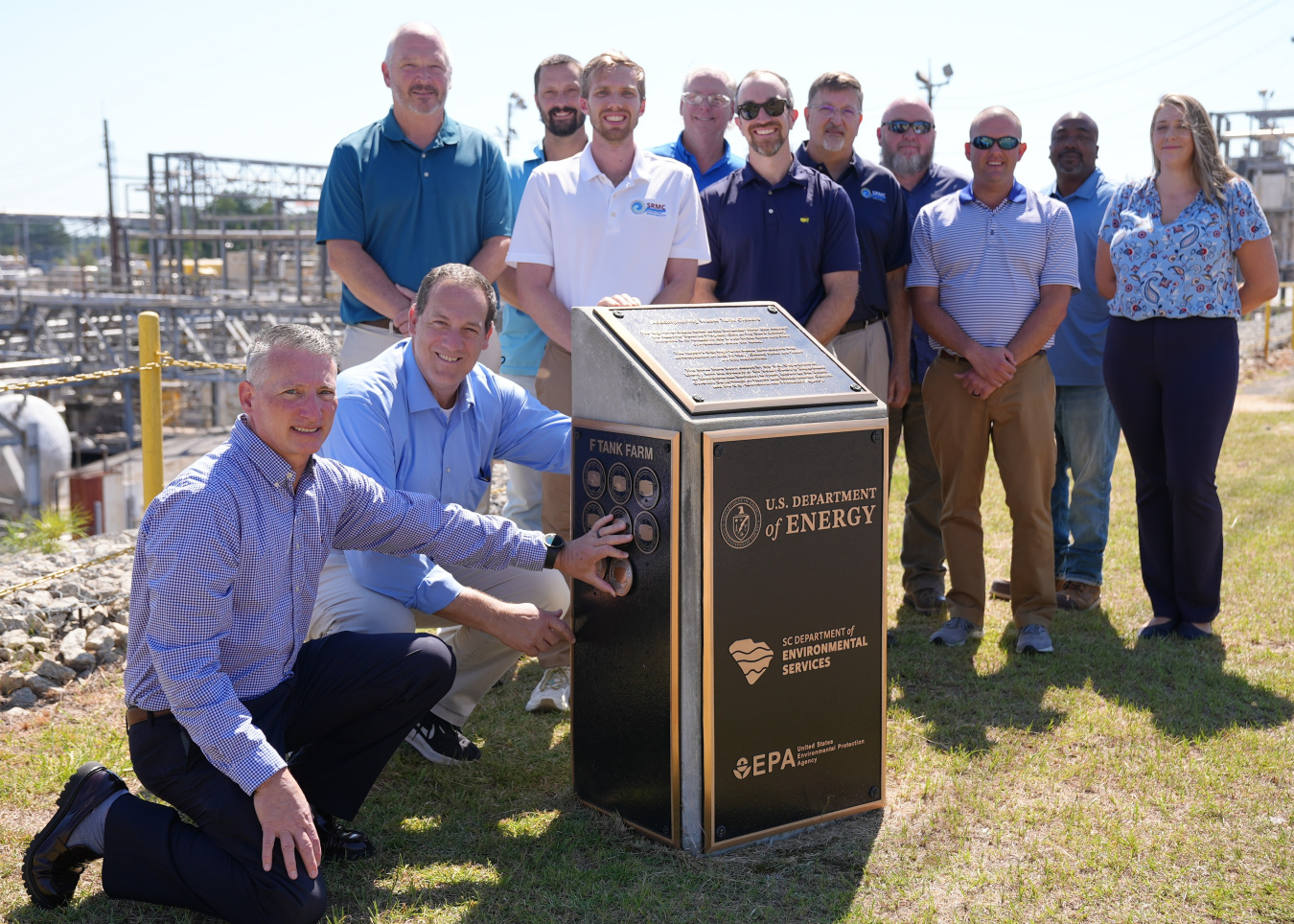 A group of professionals pose for a group photo beside a large black and gold plaque