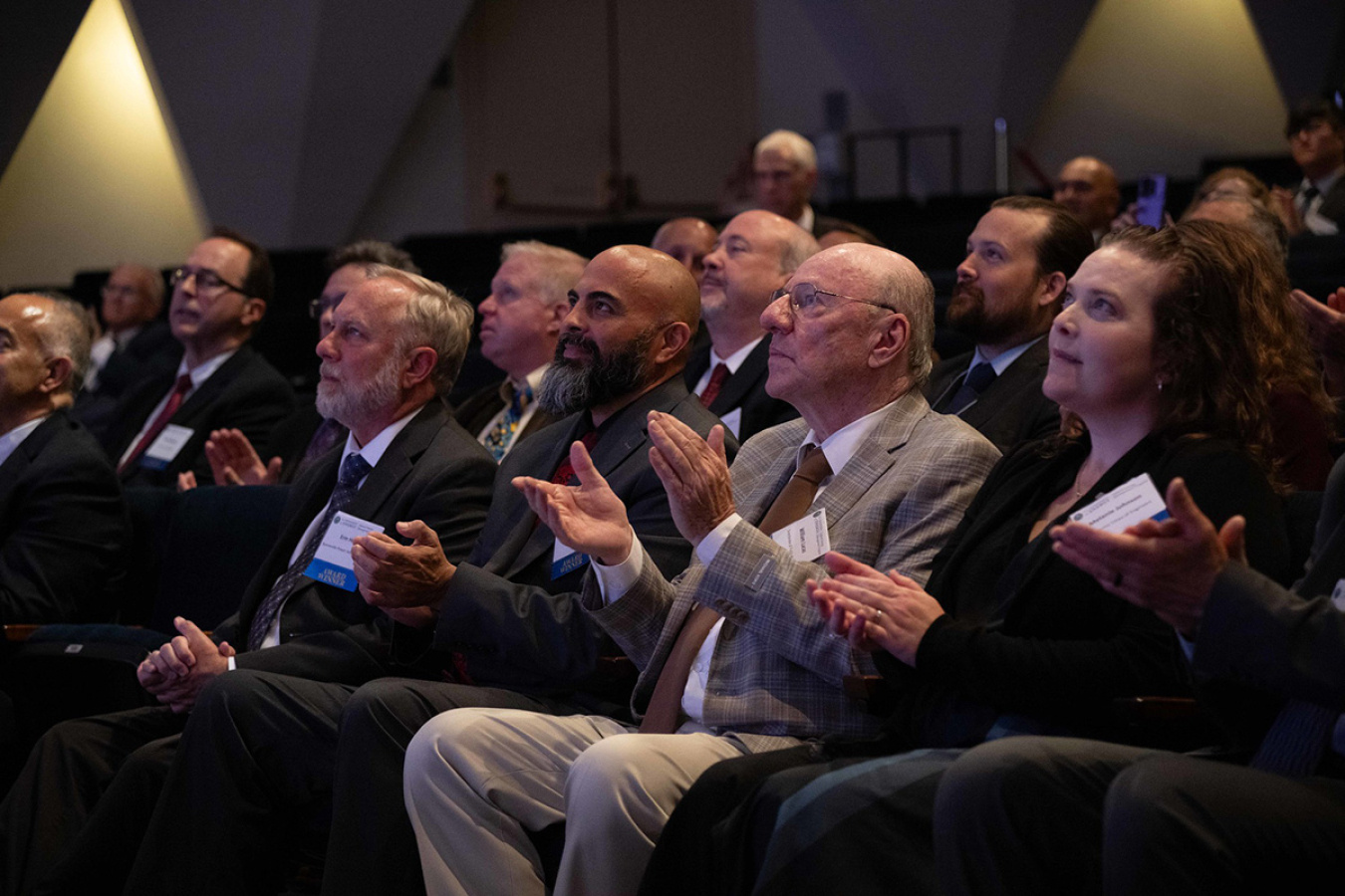 A seated audience clapping while looking at a stage (off screen).