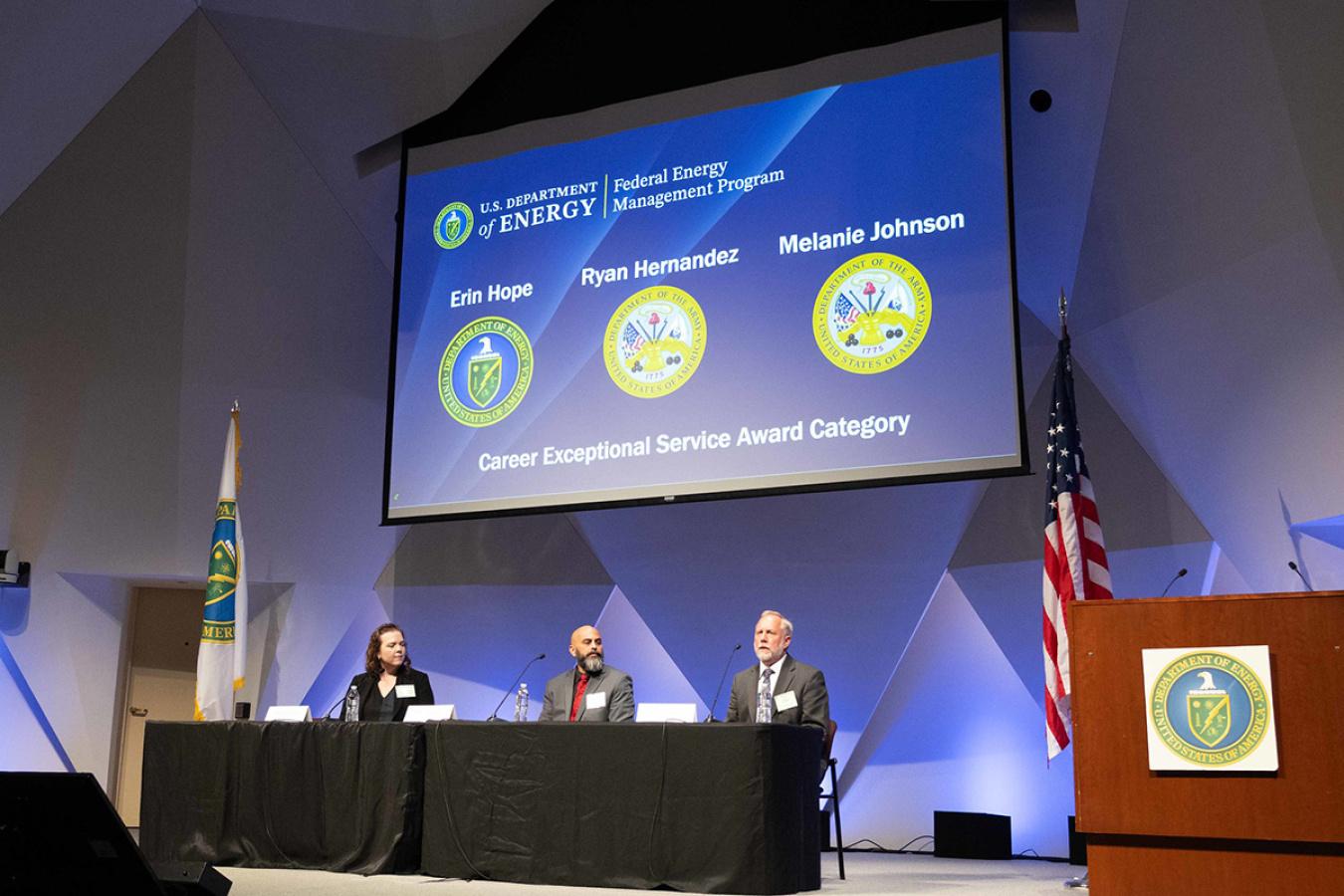 Three individuals sitting at a table on stage during a panel discussion.
