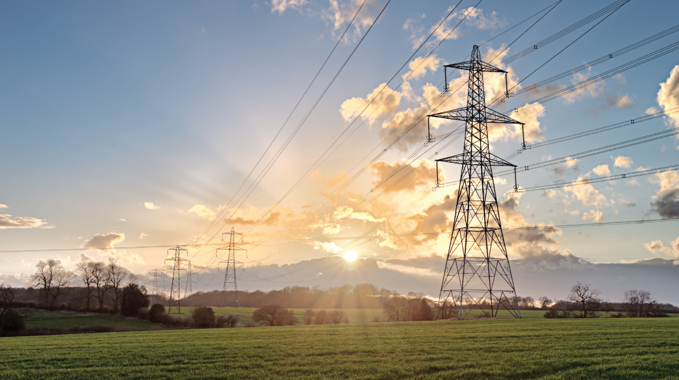 Transmission lines inside of a grassy area with cloudy skies.