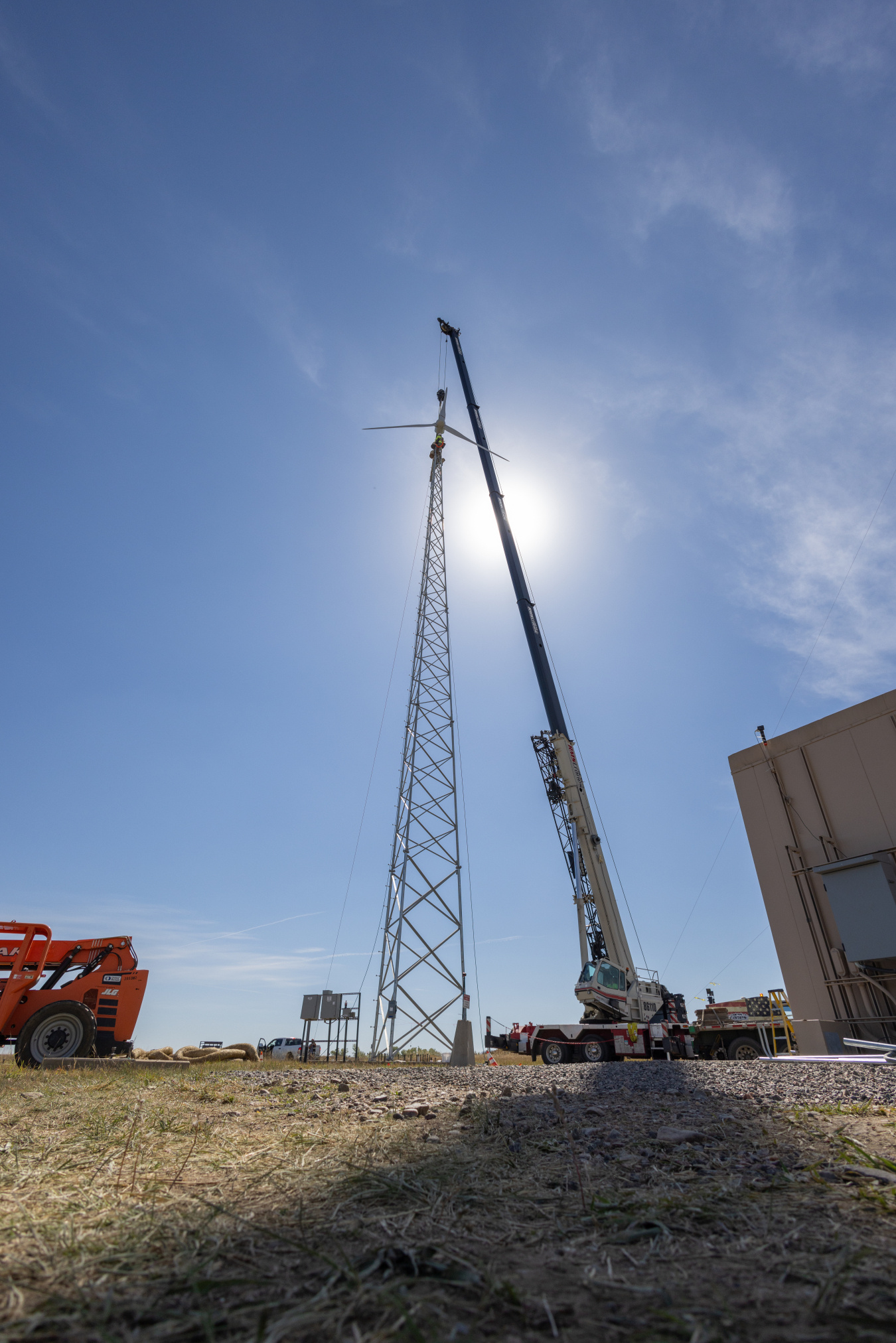 A crane lifting a rotor onto the top of a small wind turbine tower