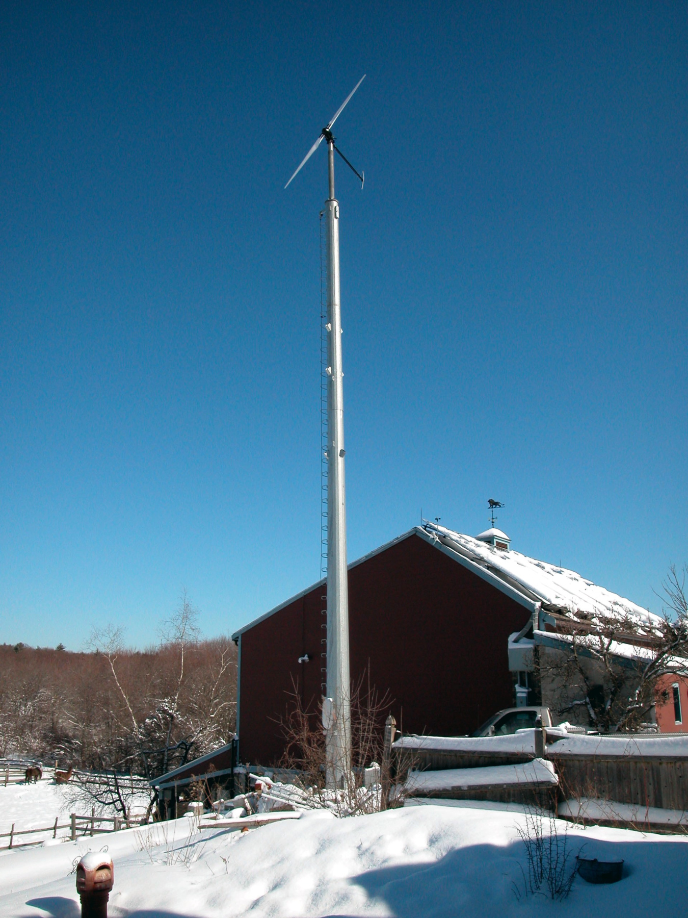 A small wind turbine next to a home in the snow.