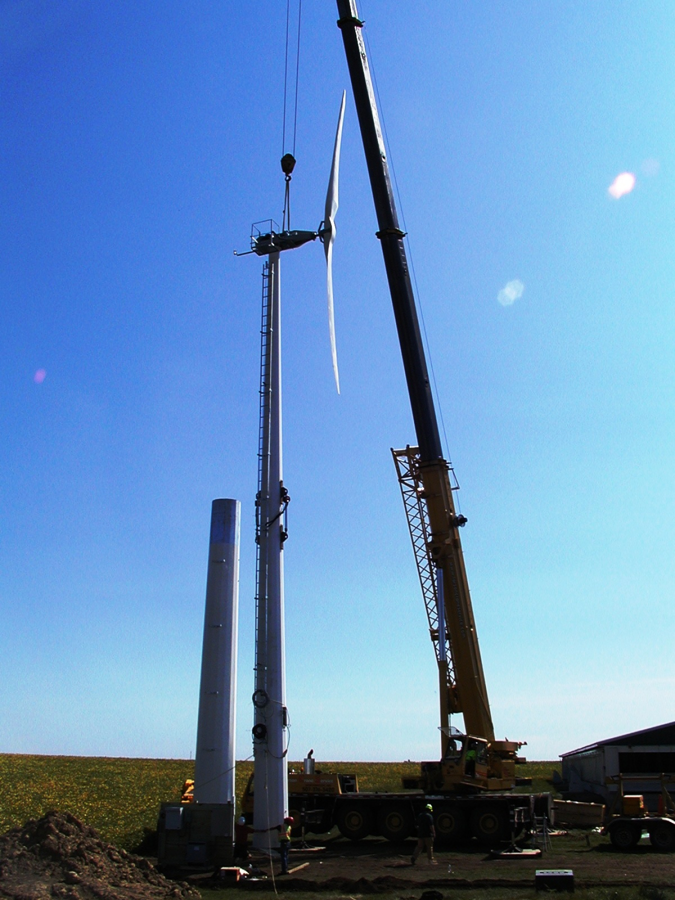 A crane lifting a two-bladed turbine rotor into place on a tower