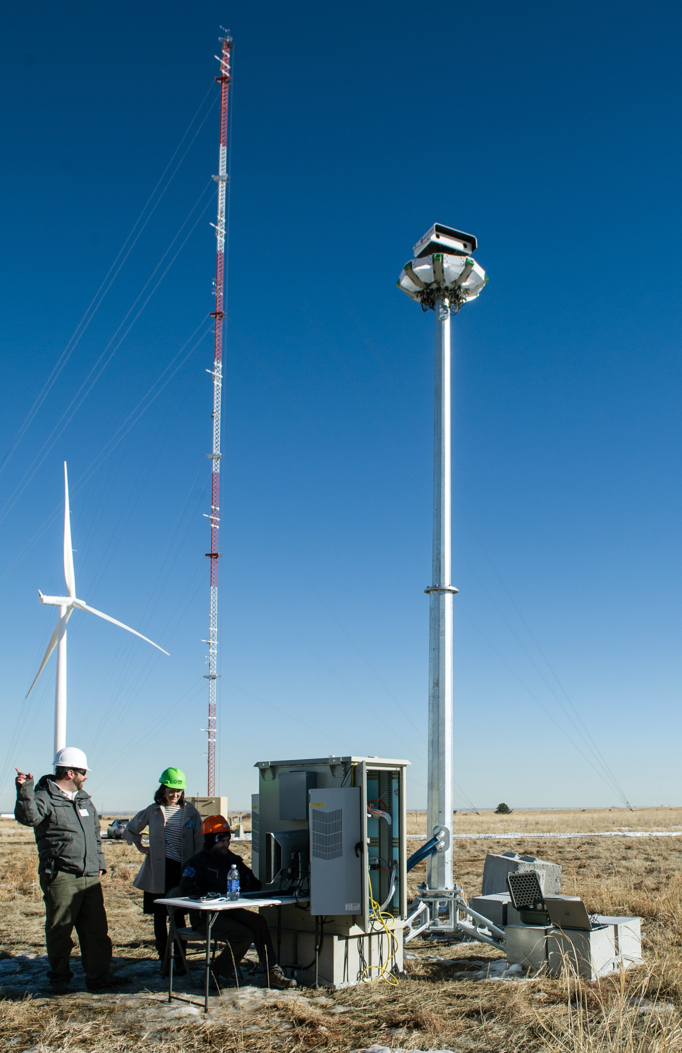 People at a table next to a radar stand in front of a wind turbine in a field