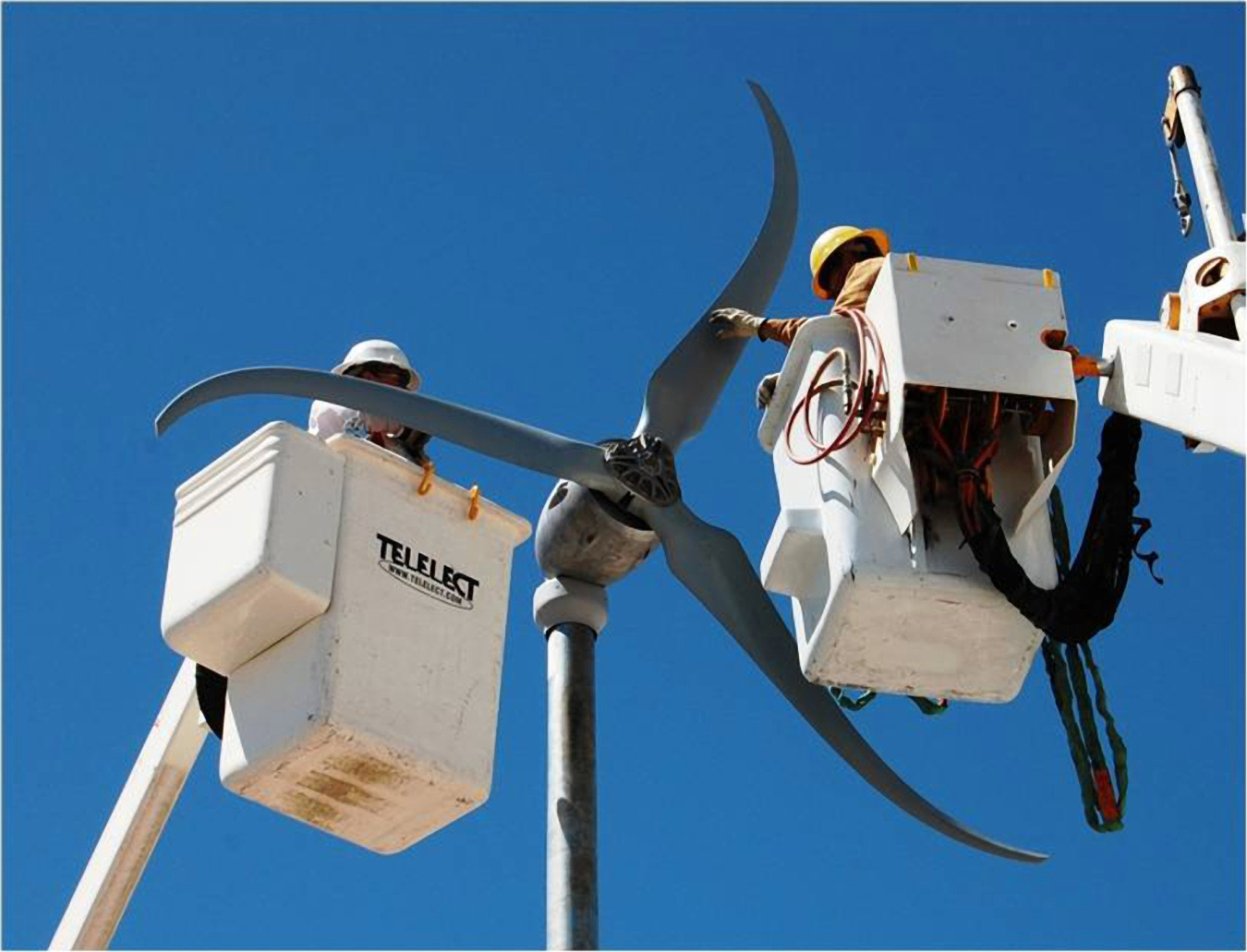 Workers in bucket lifts working on a small wind turbine's rotor