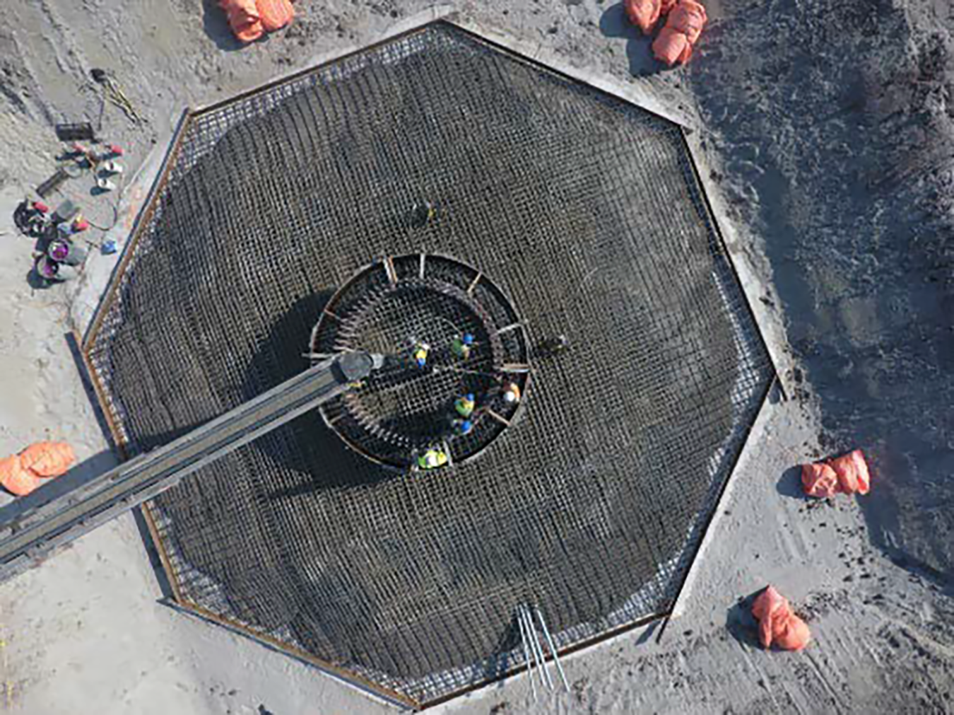 Overhead view of an octagonal base in a dug pit on which workers in protective attire walk.