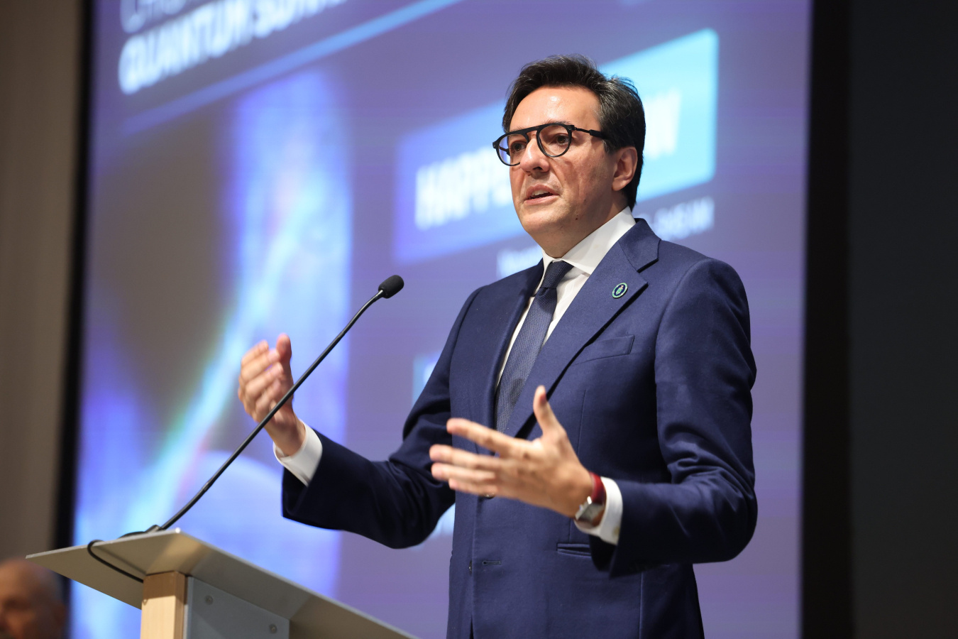 Darío Gil standing on a podium speaking with a large screen behind him. 