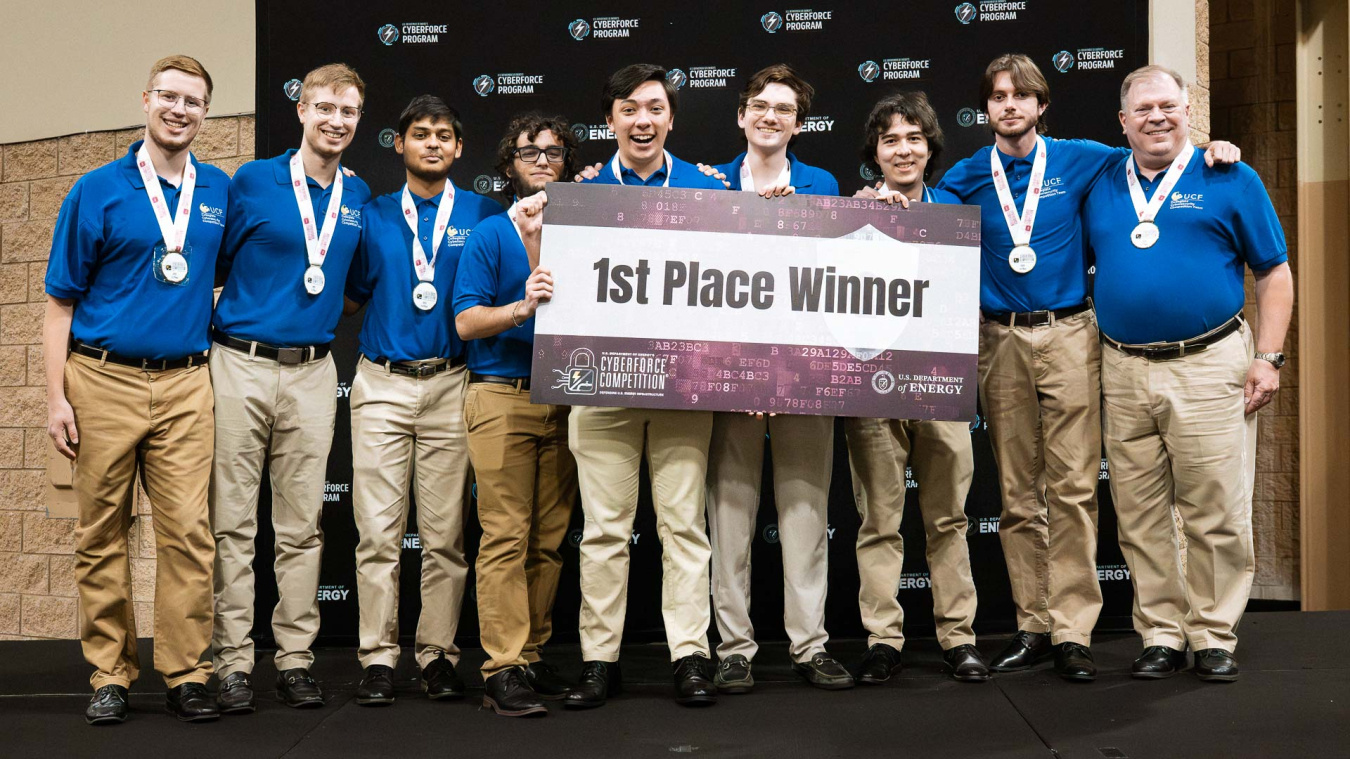 A group of students hold a sign that reads first place winner at the CyberForce Competition