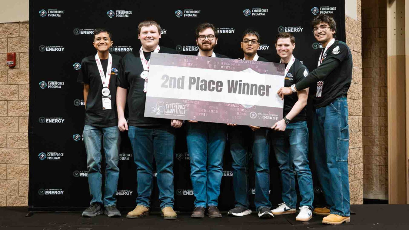 A group of students hold a sign that reads second place winner in the CyberForce Competition