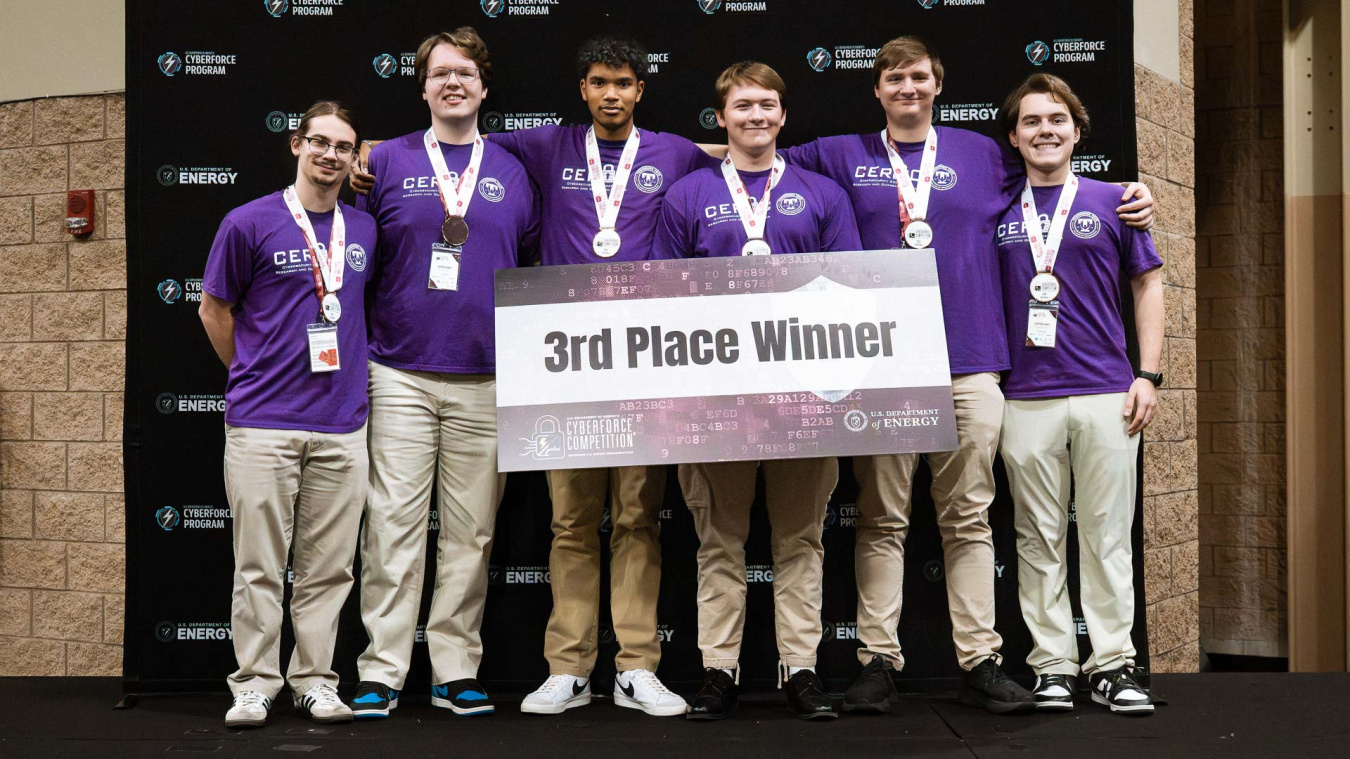 A group of students hold a sign that reads third place winner at the CyberForce Competition