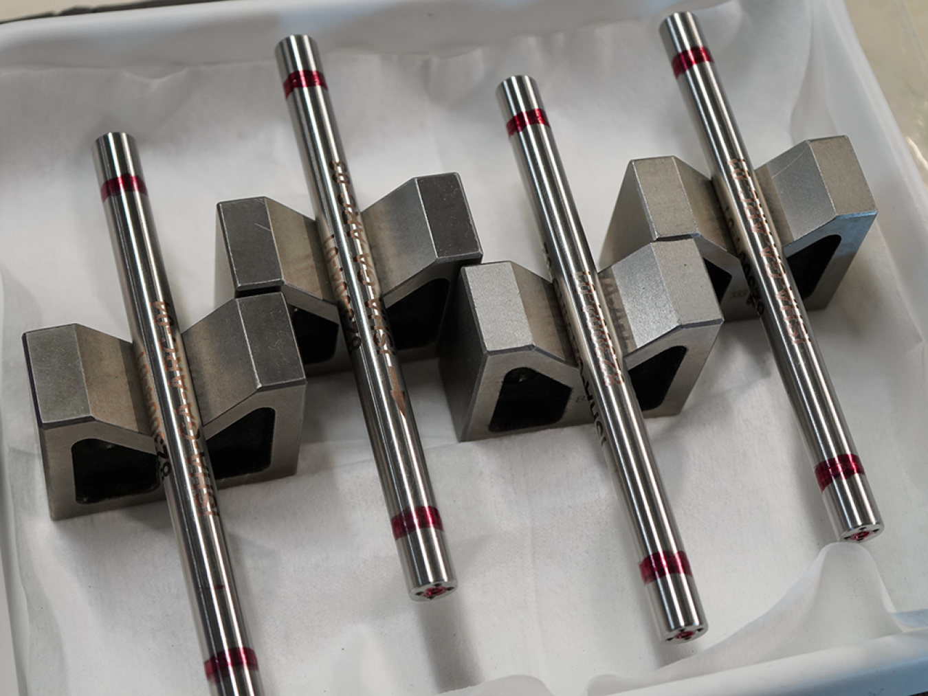 Four silver metallic fuel rod samples on display