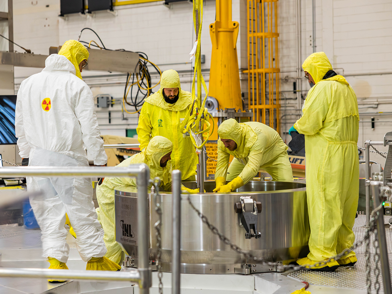 Workers in yellow protective suits load a metal cylinder into the Advanced Test Reactor.